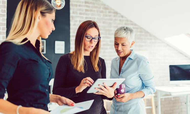 Three women reviewing information on a tablet.