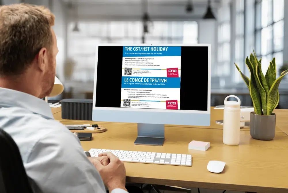 Propriétaire d'une petite entreprise en train de lire une affiche de la FCEI sur les congés de TPS/TVH sur son ordinateur