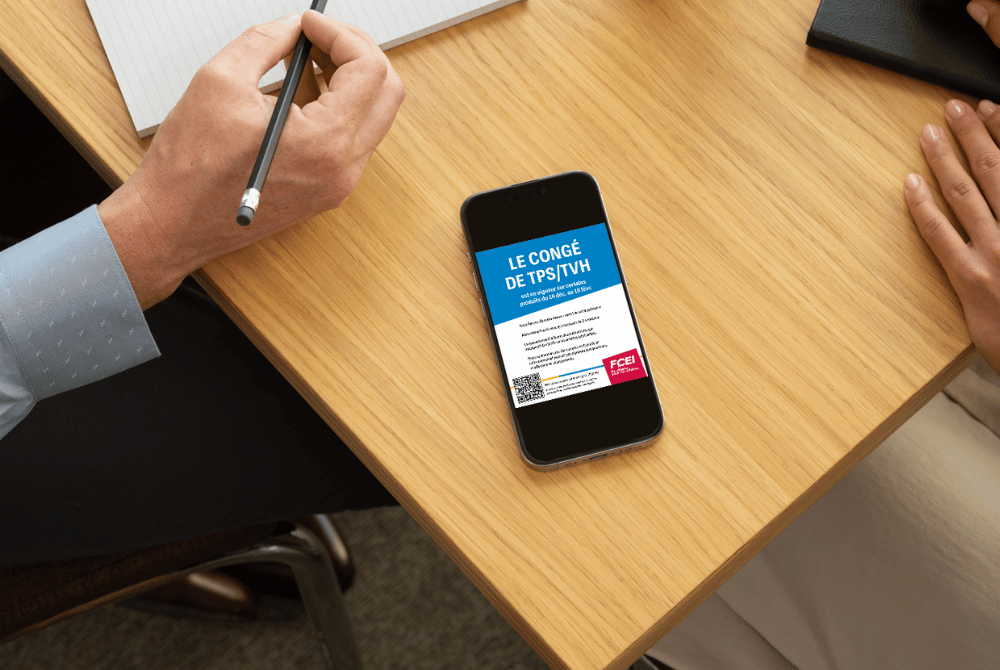 Propriétaire d'une petite entreprise en train de lire une affiche de la FCEI sur les congés de TPS/TVH sur son téléphone portable