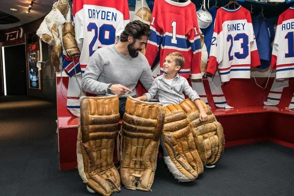 A father and son holding goalie pads inside the HHOF building