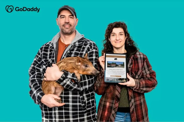 Go Daddy logo with a man holding a pig and a woman holding a tablet
