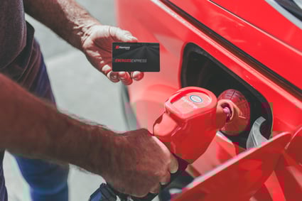 Un homme fait le plein d'essence de sa voiture tout en tenant sa carte Énergies Express.