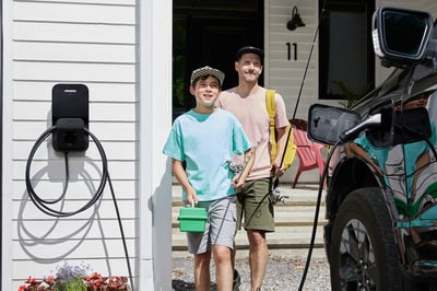 Père et fils se dirigent vers leur voiture branchée sur le chargeur de véhicule électrique.