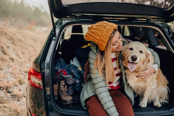 Woman hugging her dog while sitting in car trunk.