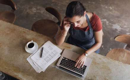 Business owner on the phone while looking at payroll paperwork on her computer