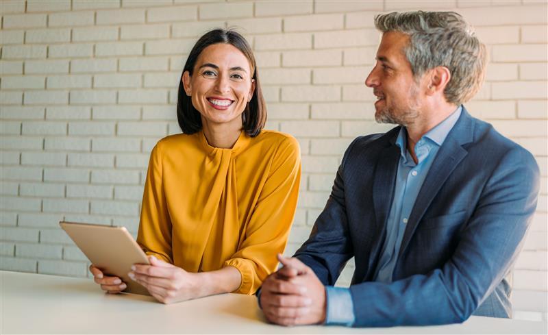 Un propriétaire d'entreprise souriant lors d'une réunion avec un autre propriétaire d'entreprise utilisant une tablette