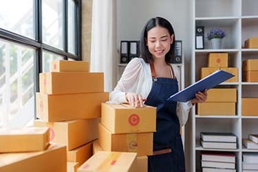 A young East Asian woman affixes a label to one of many packages