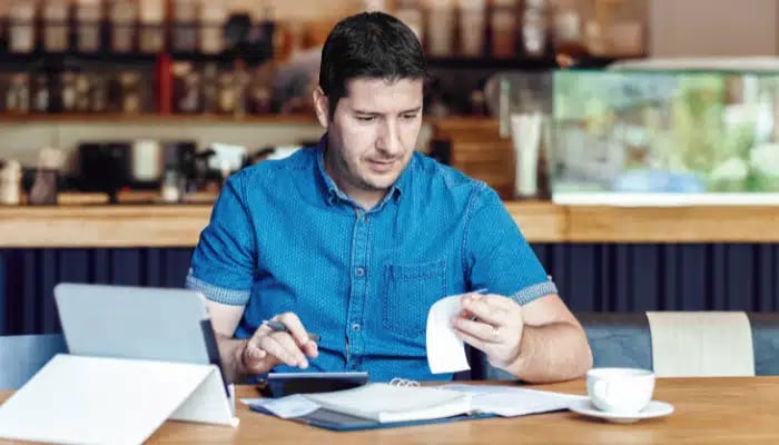 Small business owner checking his bills using a calculator