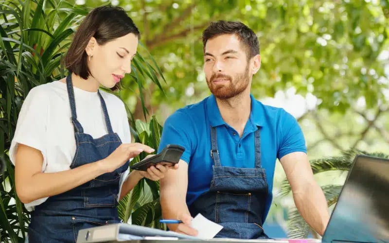 Two small business owners calculating their costs with a calculator
