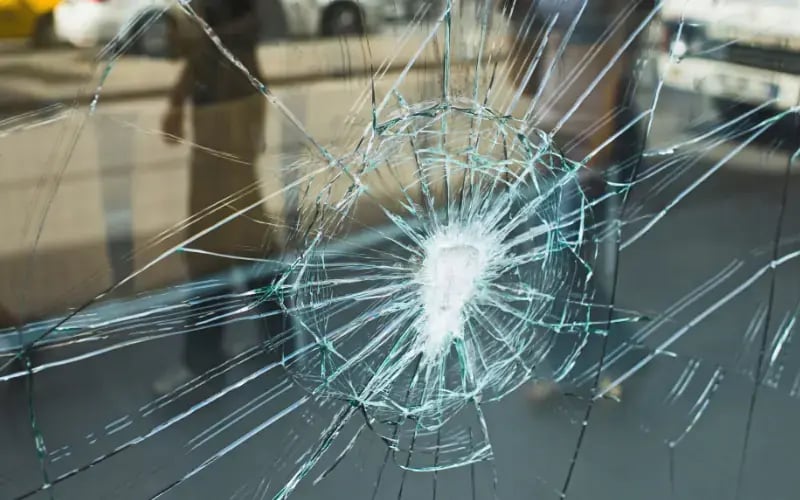 Shattered glass with a spiderweb crack pattern and a blurred street and vehicle background.