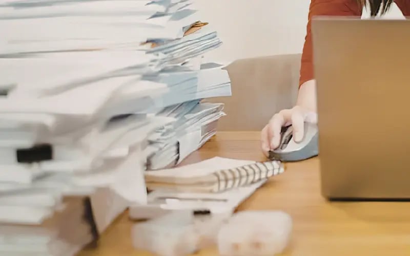 Petite entrepreneure dans sa boutique, avec des piles de paperasse sur son bureau, symbolisant la lourdeur administrative