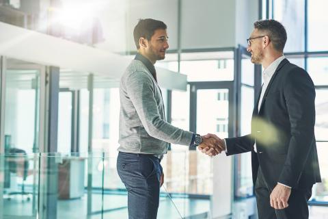 Two business men shake hands in the lobby of an office building
