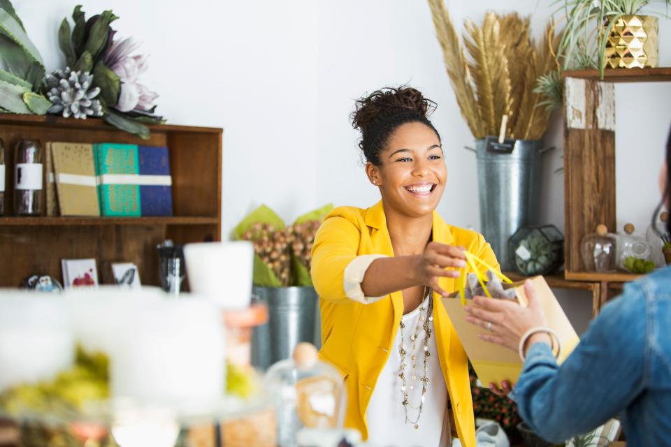 Woman passing purchased goods in a bag to her customer.