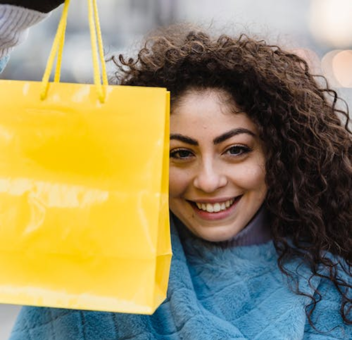 Smiling women in her twenties proudly holds up a bright yellow shopping bag