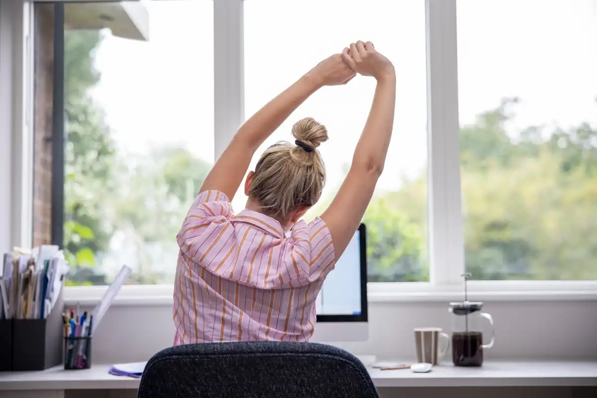 a blonde woman sitting at her desk and stretching.
