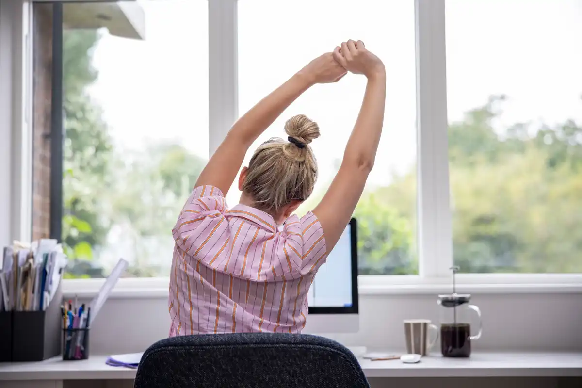 Une entrepreneure assise à son bureau fait des étirements.