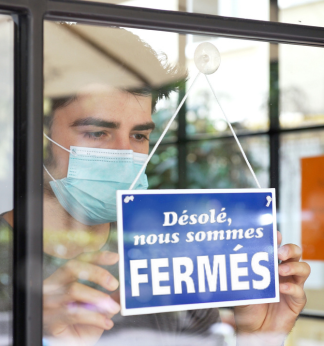 Pendant la pandémie, un entrepreneur portant un masque accroche dans la vitrine de sa boutique une affiche sur laquelle il est indiqué « Désolé, nous sommes fermés ».