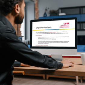 An image of a man sitting at a desktop computer with the CFIB Employee Handbook Template open on the screen. 