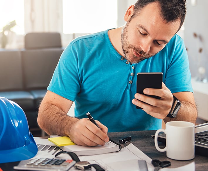 Man looking at mobile phone and recording notes