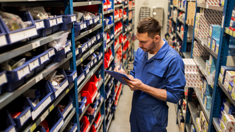employees browsing a shelf with auto parts holding a clipboard