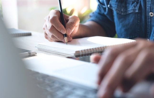 Person taking notes down on paper from a computer