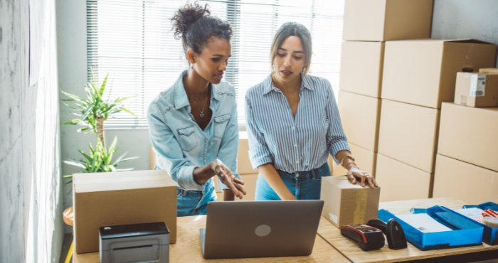 Small business women in a storage room reacting to information on a computer