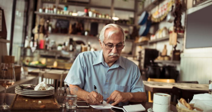 older business man doing manual calculations in a cafe