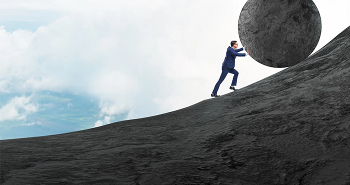 Businessman in a suit pushing a large boulder uphill, representing the burden of payroll taxes