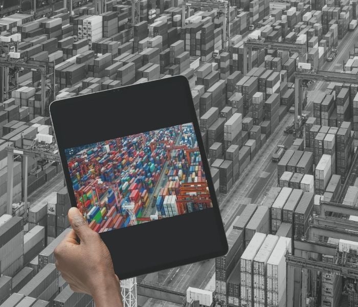 Personne dans un port tenant une tablette montrant l'image du port avec des conteneurs