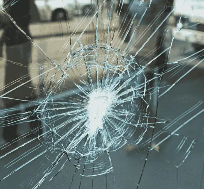 Shattered glass with a spiderweb crack pattern and a blurred street and vehicle background.