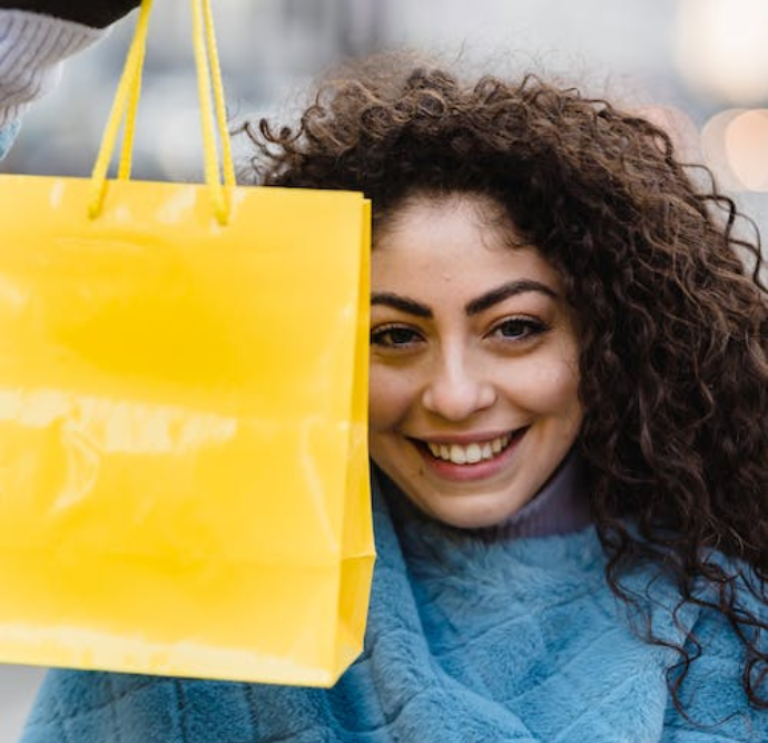 Smiling women in their twenties proudly holds up a bright yellow shopping bag.