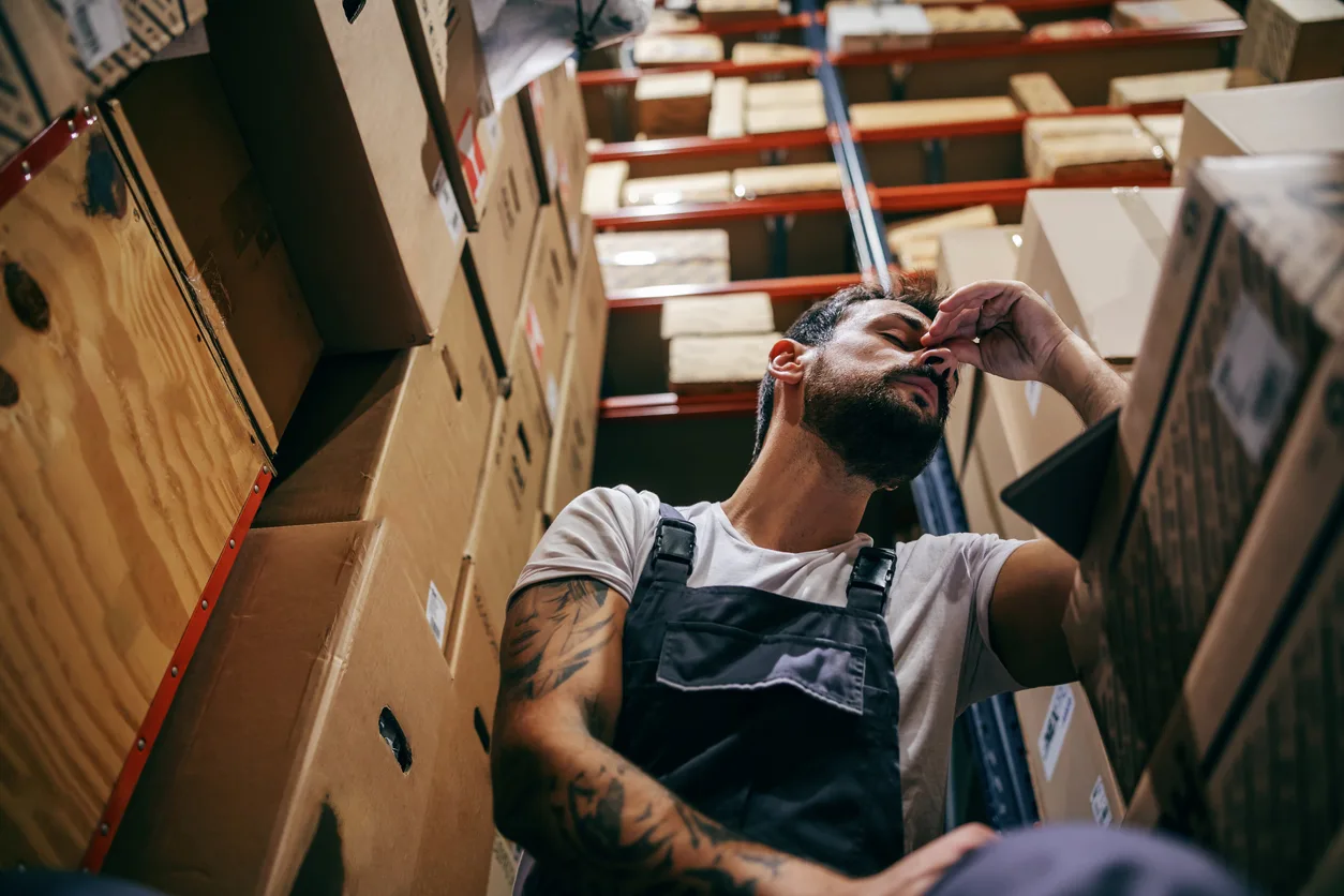 Exhausted man alone in a warehouse surrounded by boxes
