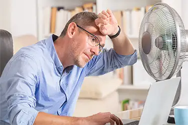 Man in office using fan to cool off